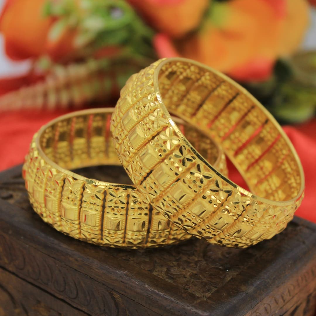 Traditional gold bangles with intricate patterns displayed on marble surface
